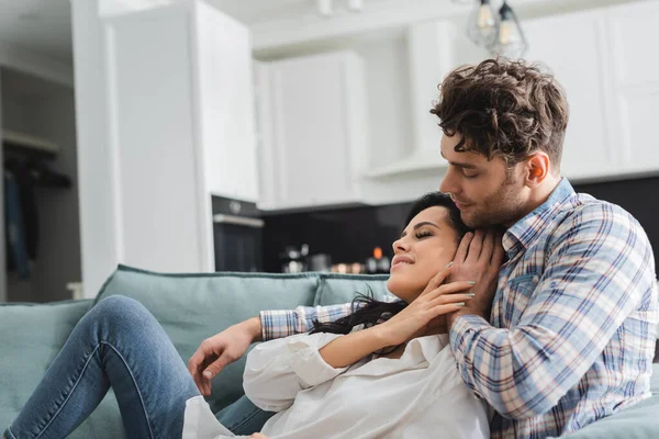 Bel homme étreignant et touchant cheveux de belle petite amie souriante sur canapé — Photo de stock