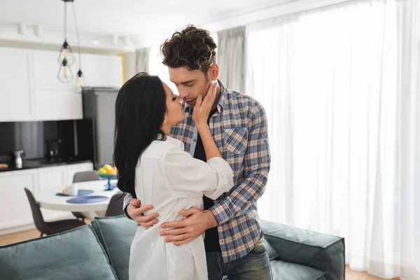 Beautiful woman kissing and hugging boyfriend in living room — Stock Photo