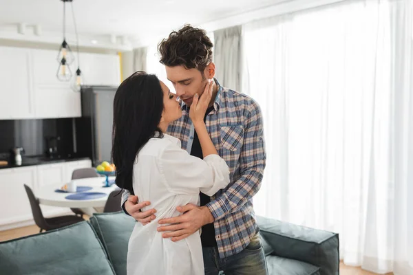 Schöne Frau küsst und umarmt Freund im Wohnzimmer — Stockfoto