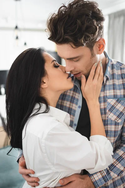 Attractive girl kissing and touching cheek of boyfriend at home — Stock Photo