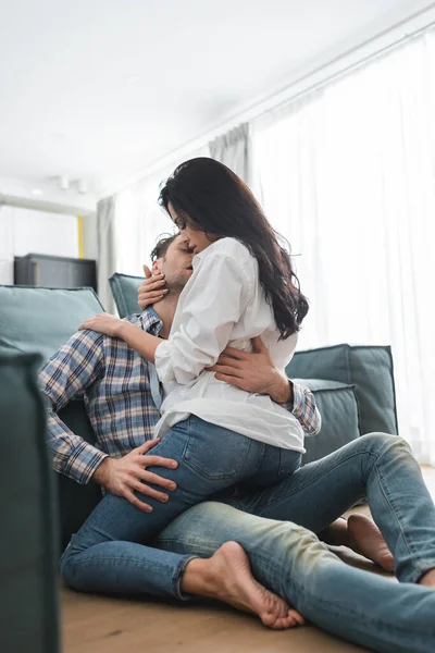 Focus selettivo della donna sensuale che abbraccia il fidanzato sul pavimento vicino al divano a casa — Foto stock