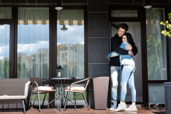 Молода пара обіймається на терасі біля будинку вдень — стокове фото