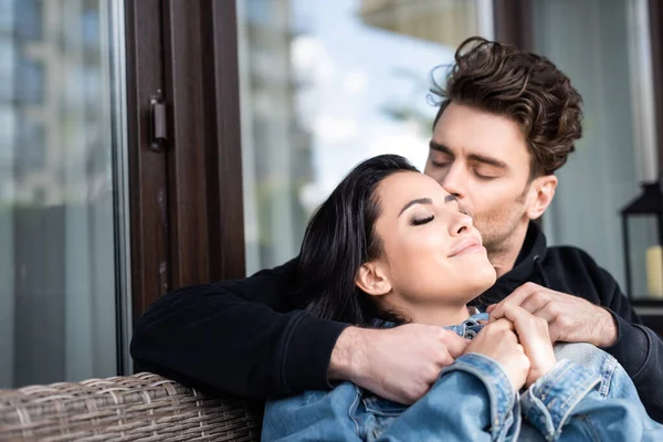 Foco seletivo do homem beijando menina atraente no sofá de vime no terraço — Fotografia de Stock