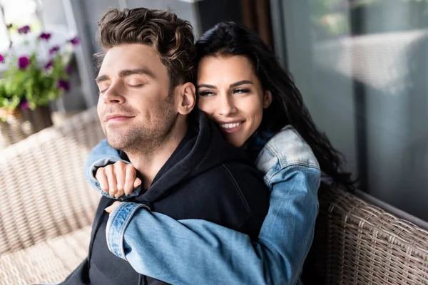 Beautiful smiling girl hugging handsome boyfriend on wicker sofa on terrace — Stock Photo