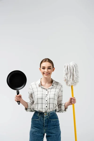 Chica sonriente posando como marioneta con fregona y sartén aislada en gris - foto de stock