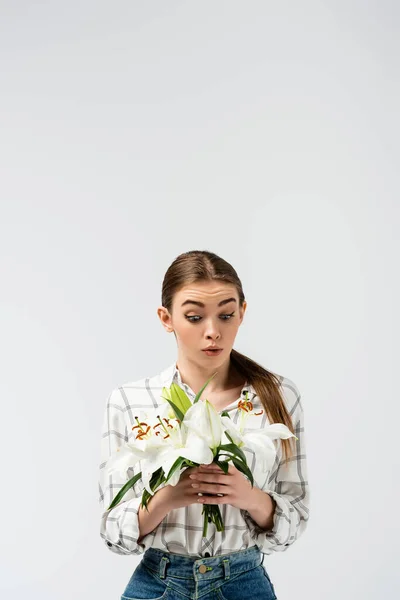 Impactado chica atractiva posando como marioneta con flores aisladas en gris - foto de stock