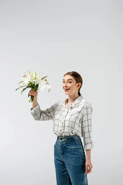 Glücklich attraktives Mädchen posiert wie eine Puppe mit Blumen isoliert auf grau — Stockfoto