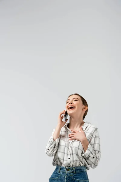 Happy attractive girl laughing while talking on smartphone isolated on grey — Stock Photo