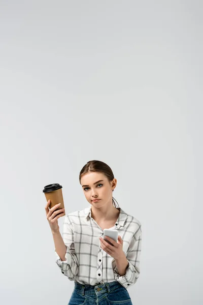 Menina cético com smartphone e café para ir isolado em cinza — Fotografia de Stock