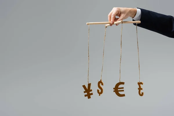 Cropped view of businessman holding currency signs on strings isolated on grey — Stock Photo
