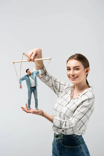 Lächelnde weibliche Puppenspielerin hält männliche Marionette isoliert auf grau — Stockfoto