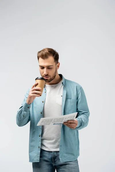 Junger Mann liest Zeitung und trinkt Kaffee isoliert auf grau — Stockfoto