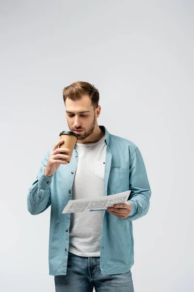 Young man reading newspaper and drinking coffee isolated on grey — Stock Photo