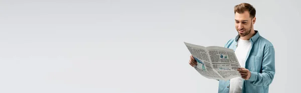 Улыбающийся молодой человек, читающий газету изолированный на сером, панорамный снимок — стоковое фото