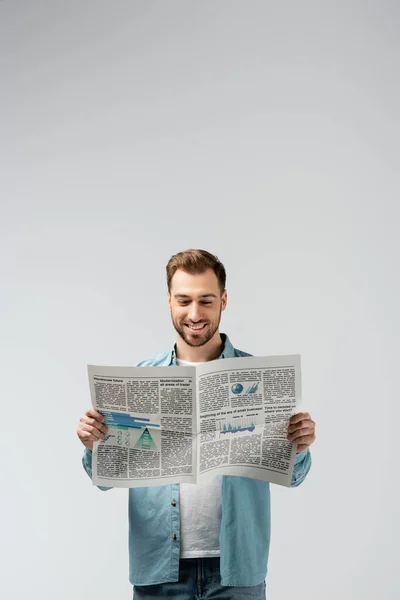 Улыбающийся молодой человек, читающий газету, изолированную от серых — стоковое фото