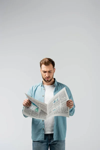 Confused young man reading newspaper isolated on grey — Stock Photo