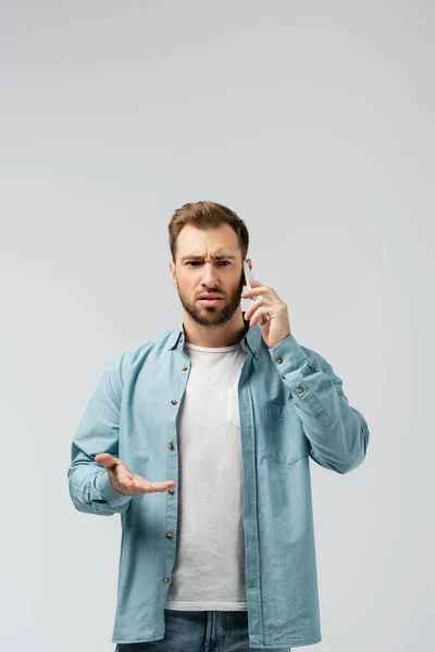 Verwirrter junger Mann spricht auf Smartphone isoliert auf grau — Stockfoto