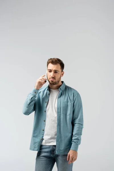Грустный молодой человек разговаривает на смартфоне изолирован на серый — стоковое фото
