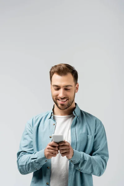 Smiling young man using smartphone isolated on grey — Stock Photo