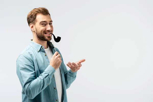 Divertente giovane uomo con falsa pipa di tabacco isolato su grigio — Foto stock