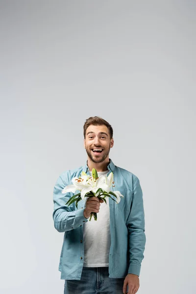 Happy young man with floral bouquet isolated on grey — Stock Photo