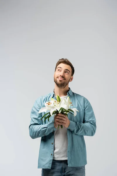 Мечтательный молодой человек с цветочным букетом изолирован на сером — стоковое фото