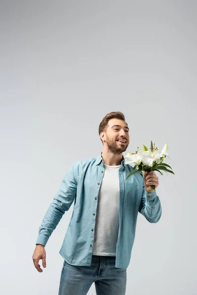 Happy young man with floral bouquet isolated on grey — Stock Photo