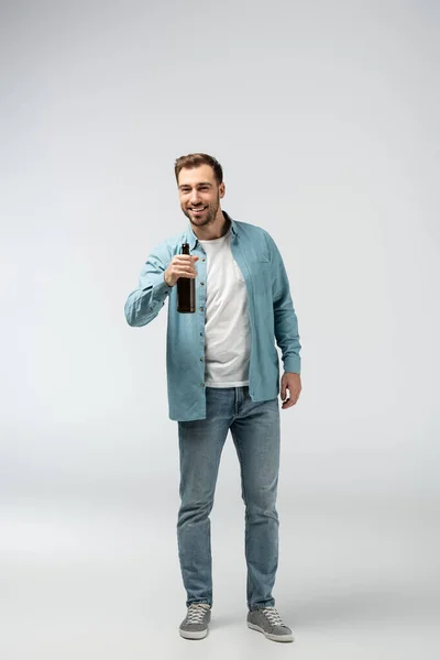Lächelnder junger Mann mit Bierflasche in grau — Stockfoto