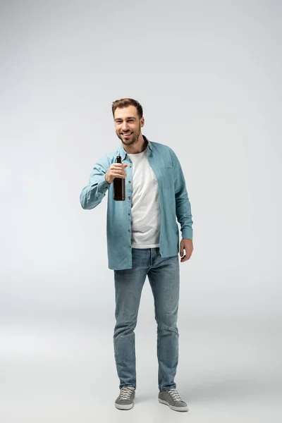 Jeune homme souriant avec bouteille de bière isolée sur gris — Photo de stock