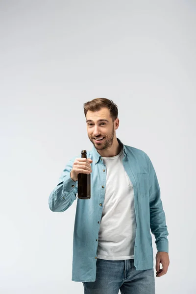 Улыбающийся молодой человек с бутылкой пива, изолированной на сером — стоковое фото