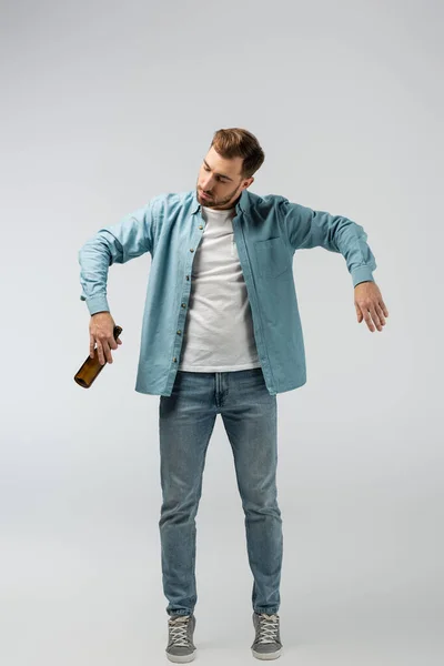 Young man posing like puppet with bottle of beer isolated on grey — Stock Photo