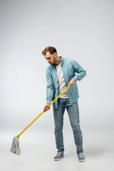 Сумний молодий чоловік прибирає підлогу з мопедом ізольовано на сірому — стокове фото