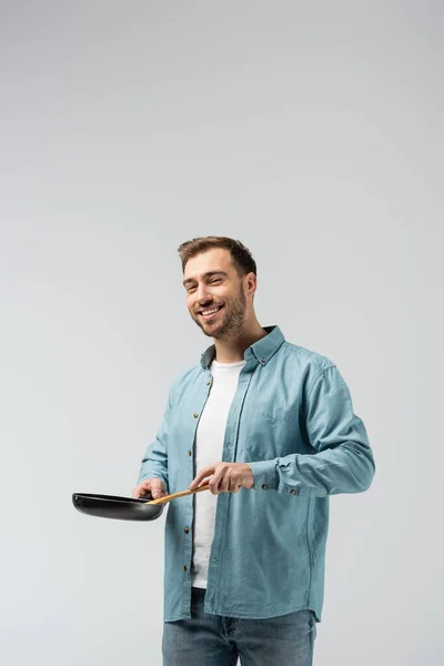 Усміхнений молодий чоловік зі сковородою і шпателем ізольований на сірому — стокове фото