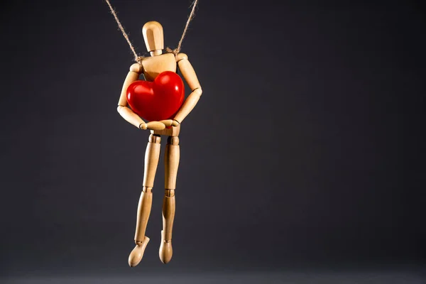 Wooden marionette on strings with red heart isolated on black — Stock Photo