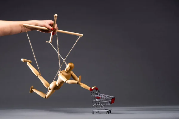 Cropped view of puppeteer holding wooden marionette with shopping cart on black — Stock Photo