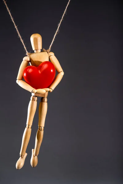 Marioneta de madera en cuerdas con corazón rojo aislado en negro - foto de stock