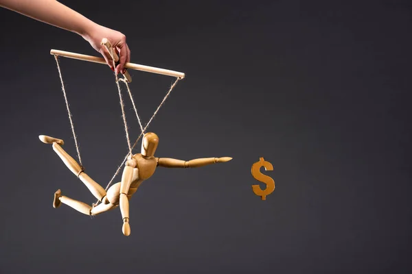 Cropped view of puppeteer holding wooden marionette near dollar sign isolated on black — Stock Photo