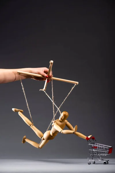 Cropped view of puppeteer holding wooden marionette with shopping cart on black — Stock Photo