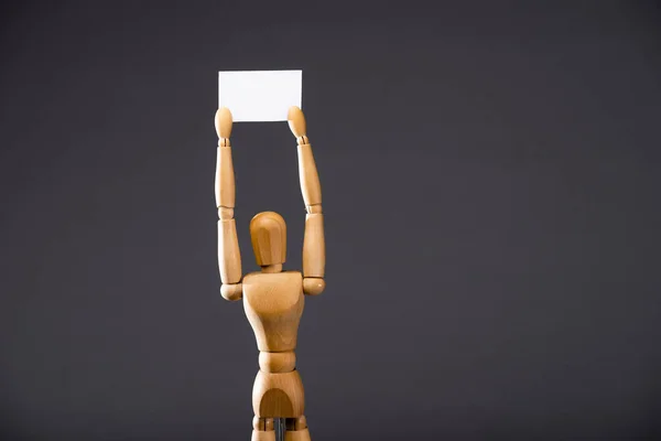 Marioneta de madera sosteniendo pancarta en blanco sobre fondo negro - foto de stock