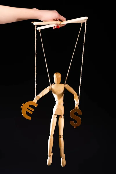 Cropped view of puppeteer holding wooden marionette on strings with currency signs isolated on black — Stock Photo