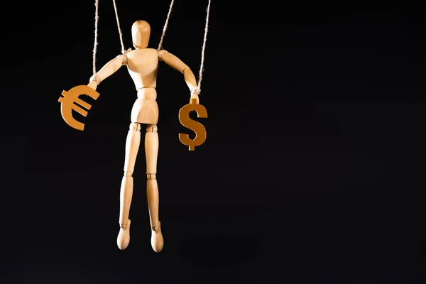 Wooden marionette on strings holding currency signs isolated on black — Stock Photo