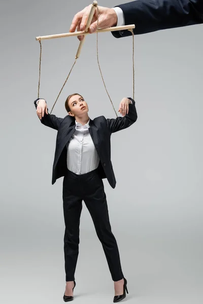 Cropped view of puppeteer holding businesswoman marionette on strings isolated on grey — Stock Photo