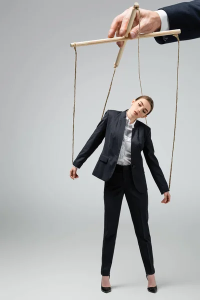 Cropped view of puppeteer holding businesswoman marionette on strings isolated on grey — Stock Photo
