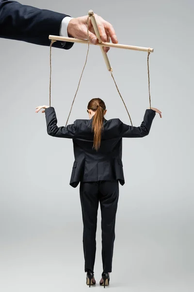 Cropped view of puppeteer holding businesswoman marionette on strings isolated on grey — Stock Photo