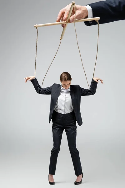 Vista recortada del titiritero sosteniendo marioneta empresaria en cuerdas aisladas en gris - foto de stock