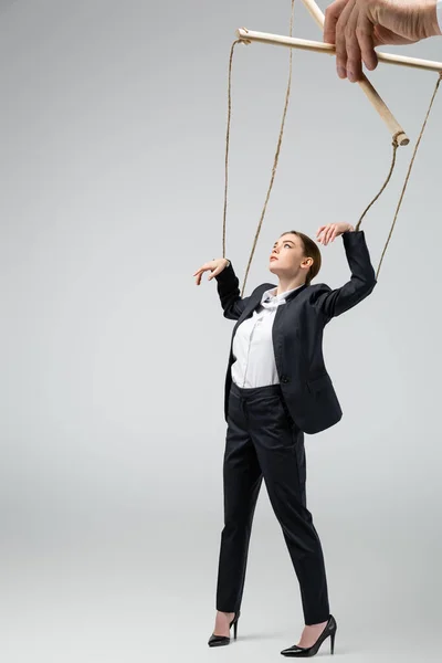 Cropped view of puppeteer holding businesswoman marionette on strings isolated on grey — Stock Photo