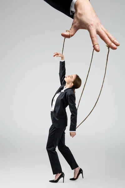 Vista cortada de marionete fantoche segurando empresária em cordas isoladas em cinza — Fotografia de Stock