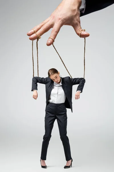 Cropped view of puppeteer holding businesswoman marionette on strings isolated on grey — Stock Photo