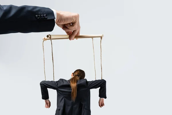 Vista recortada del titiritero sosteniendo marioneta empresaria en cuerdas aisladas en gris - foto de stock
