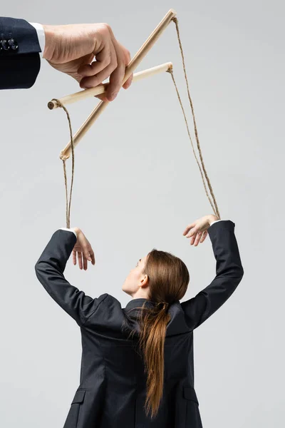 Vista recortada del titiritero sosteniendo marioneta empresaria en cuerdas aisladas en gris - foto de stock